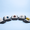 A collection of trucker caps in beige and black, each featuring different logos on the front.