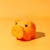An orange piggy bank with black eyes on a yellow background. The piglet has a rounded shape and a glossy finish.