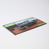 A square cut fridge magnet featuring a vintage black car on a dirt road with a logo in the corner.