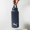 A drink bottle in dark blue with a handle and a logo on the front, suspended by a hand.
