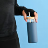 A drink bottle with a blue exterior, clear top, and bamboo lid, featuring a straw and held by a person.