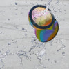 A colourful, reusable water balloon splashes through water droplets against a grey background.
