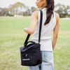 A black cooler bag with a shoulder strap and mesh pocket, being carried by a person in a casual outfit.