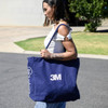 A navy tote bag with a logo, featuring sturdy handles and a spacious design, carried by a person.