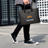 A nylon briefcase in black being carried by a person wearing black jeans and sneakers, featuring a logo.