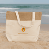 A jute and cotton cooler bag in beige with a logo on the front, set against a beach background.