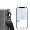 A black tracking tag attached to a grey material, alongside a smartphone displaying a map interface.