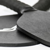 A black pickleball paddle and ball set with a textured grip, featuring a logo on one item.