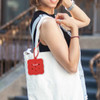 A red square silicone pouch with holes attached to a white tote bag. It features a small logo on the pouch.