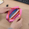 A pink silicone pencil case with an orange zipper, containing various pens and a USB drive inside.