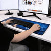 A rubber desk mat with a blue cityscape design, placed beneath a keyboard on a workspace.