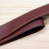 A brown faux leather strap with contrasting yellow stitching, laid flat on a wooden surface.