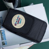A black phone pouch with a belt clip, featuring a circular patch with a logo, resting on books and a bottle.