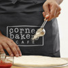 A dark grey waist apron features a logo, with a person using a scoop above a pizza dough.