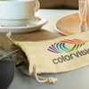 A cotton drawstring pouch in natural colour containing sunglasses, paired with a coffee cup and a wooden plate.