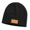 A dark grey cable knit beanie featuring a patch on the front. The beanie has a ribbed texture.