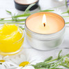 A silver tin candle with a lit amber-wax flame, surrounded by yellow gel and fresh flowers.
