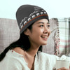 A grey custom knitted beanie with a mountain and bear design, worn by a smiling person holding a drink.