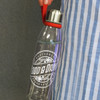 A drink bottle with a transparent glass body, silver lid, and a red carrying strap, featuring a branding logo.