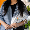 A person wearing a navy blue and white Ohau Throw Blanket with a logo on one side. The blanket features a geometric pattern.