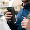 A drink bottle in matte black with a logo, held by a person in a blue shirt.