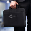 A black travel portfolio case with two handles, featuring a logo on the front, held by a person in a suit.