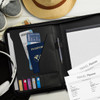 A black travel portfolio case displaying a passport, travel documents, credit cards, a pen, and notepads, alongside a hat and shoes.