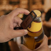A drink bottle opener key ring with a wooden finish and a logo, held over a beer bottle.