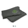 A grey herringbone throw blanket with fringed edges and a logo of a lotus flower.
