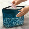 A large teal cosmetic bag with a floral design being opened to reveal a pink spray bottle inside.