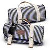 A blue and white striped picnic blanket rolled up, featuring a carrying handle and a logo tag.