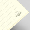 A soft cover notebook with lined pages in a pale yellow colour, featuring a logo in the bottom corner.