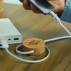 A bamboo retractable charging cable with white cords connected to a phone and portable charger on a wooden surface.