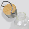 A drink bottle with a transparent glass body, topped with a rounded bamboo and metal lid, featuring a handle.