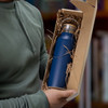 A blue drink bottle is displayed inside a die-cut box with a locking lid, surrounded by straw packing.