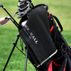 A black golf towel hangs from a golf bag, featuring a textured surface and a logo.
