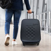 A small black wheeled suitcase with a textured surface, being pulled by a person wearing blue jeans and sneakers.