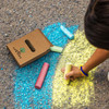 A set of jumbo sidewalk chalk pieces in various colours, with a cardboard box featuring a logo on the ground.