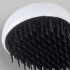 A hair detangler brush with a white handle and black bristles, featuring a round design.