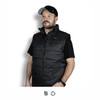 A man wearing a black puffer vest, featuring a zip closure and high collar, with a logo on the chest.
