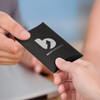A small black pillow box is being handed from one person to another, featuring a logo.