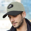 A cap in olive green with a black peak and patch, featuring a logo on the front.