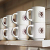 Stackable white coffee mugs displayed on a shelf, featuring a logo in brown.