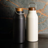 A drink bottle duo featuring a matte black and a creamy white vacuum-sealed design with wooden lids and metal handles.