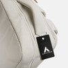 A light grey backpack with a handle and a tag attached, featuring a logo.