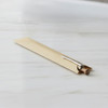 A Kraft paper pen sleeve in a beige shade, containing a silver pen with a wooden barrel, resting on a marble surface.