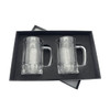 A set of two clear glass beer mugs, presented in a black gift box with a velvet interior.