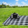 A striped black and white cooler bag sits on a checkered blanket in a grassy field under a blue sky.