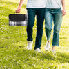 A picnic rug in a black and white check pattern, being carried by a couple walking on grass.