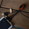 A bamboo charging cable with RPET connectors, featuring black fabric sheathing and an orange accent, on a wooden surface.